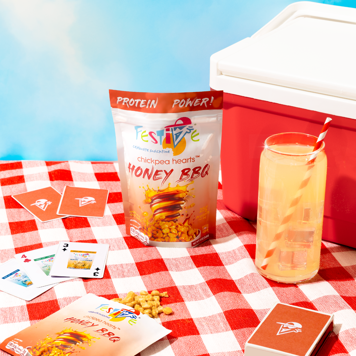 Festive chickpeas package, drink, and cards on a red and white checkered tablecloth with a cooler in the background.