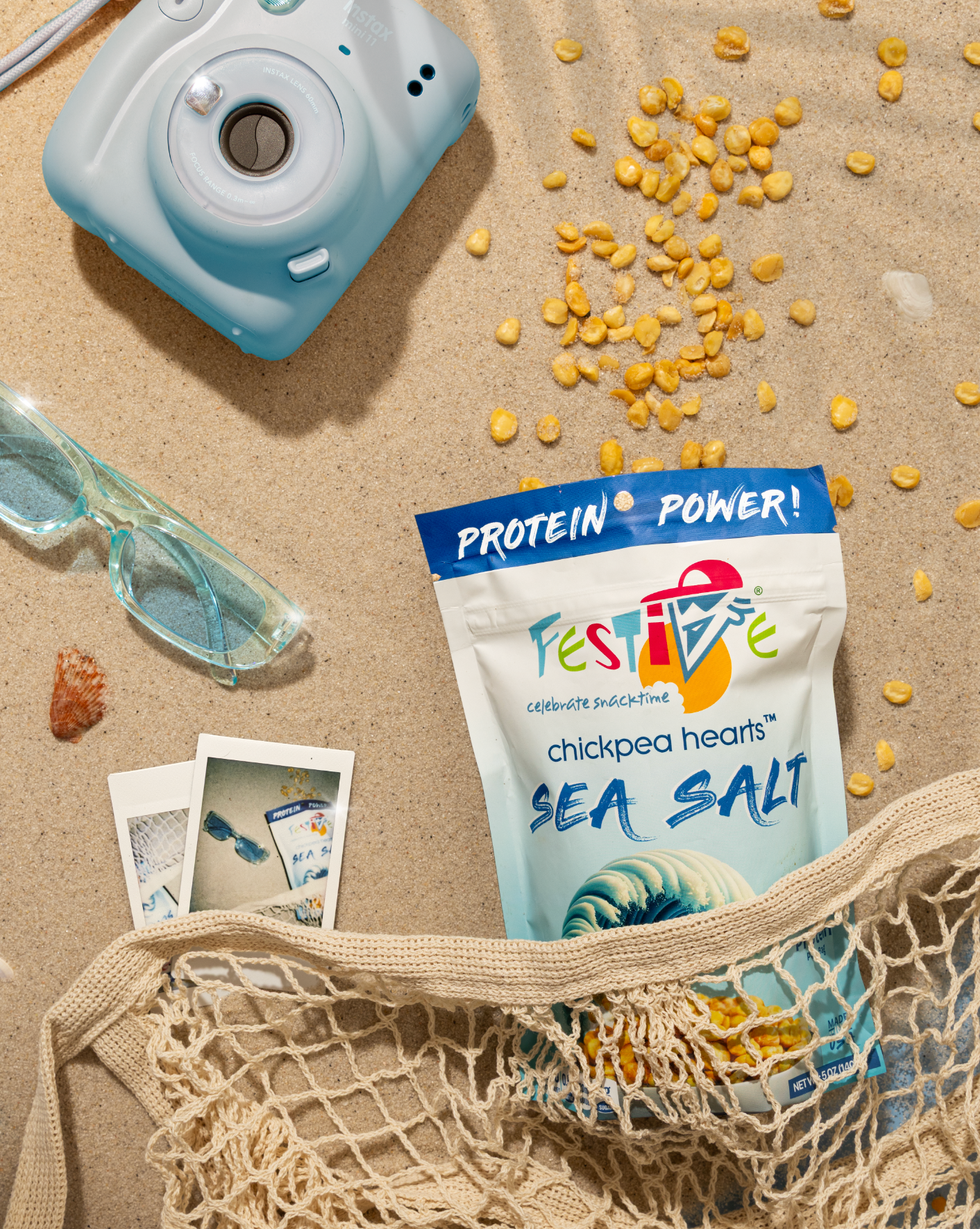 Festive Sea Salt chickpea hearts package on sand with camera, sunglasses, and photos.